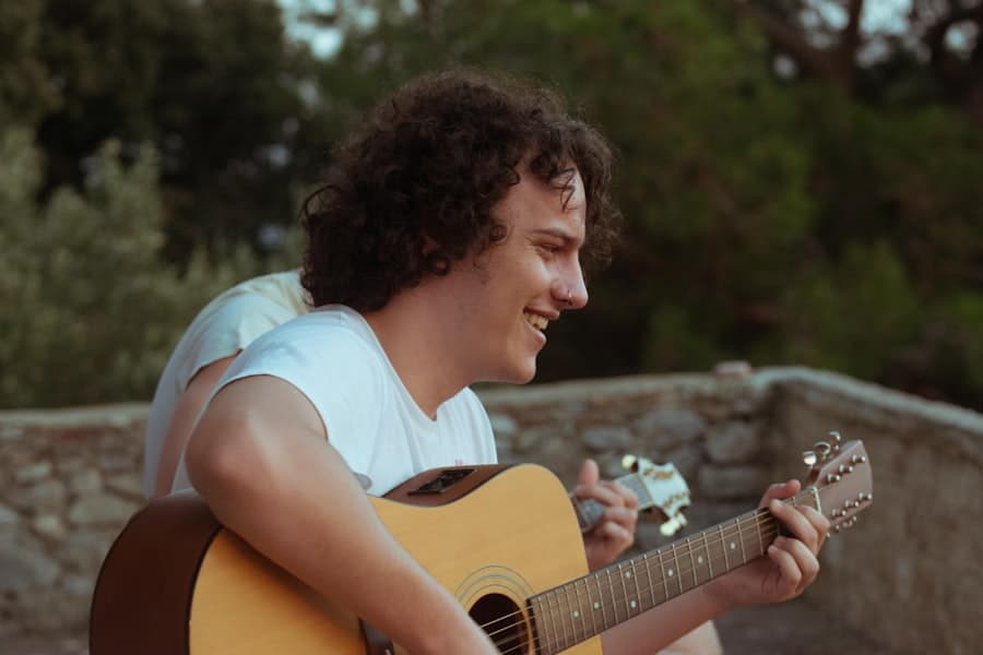 A young man smiling while playing acoustic guitar outdoors at golden hour